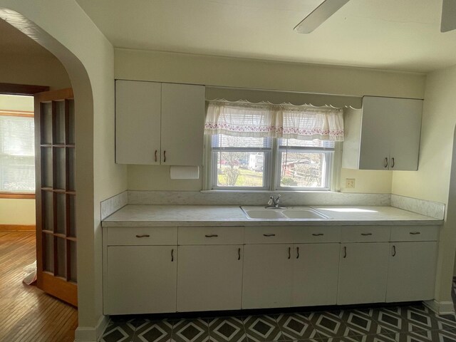 kitchen featuring arched walkways, white cabinetry, light countertops, and a sink