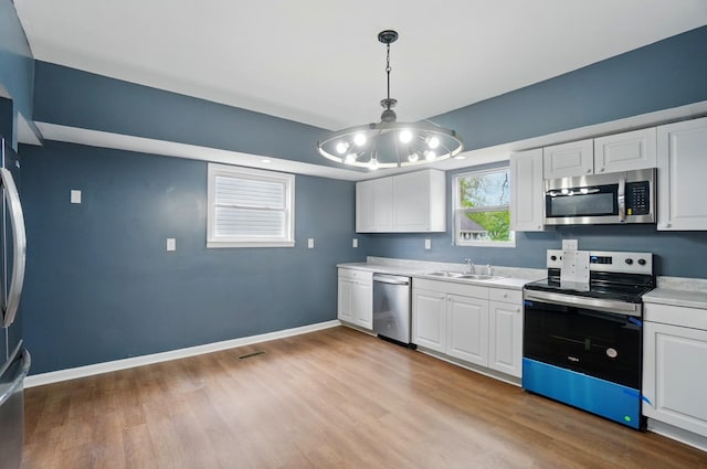 925 E St, Springfield, OH 45505 - kitchen with appliances with stainless steel finishes, light wood-type flooring, a chandelier, light countertops, and white cabinetry
