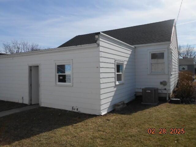 rear view of property featuring central AC unit, a lawn, and a shingled roof