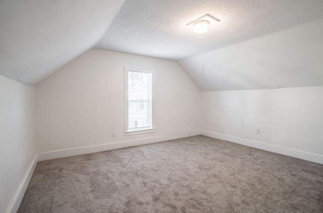 additional living space with baseboards, carpet, vaulted ceiling, and a textured ceiling