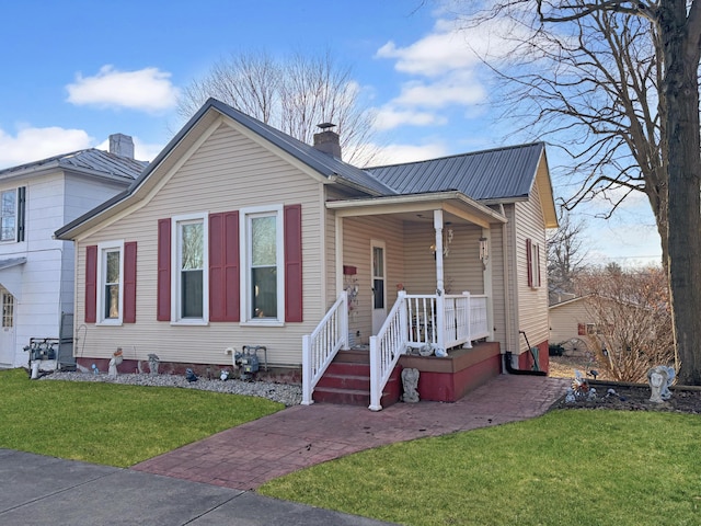 view of front of home featuring metal roof, a front lawn, a porch, and a chimney