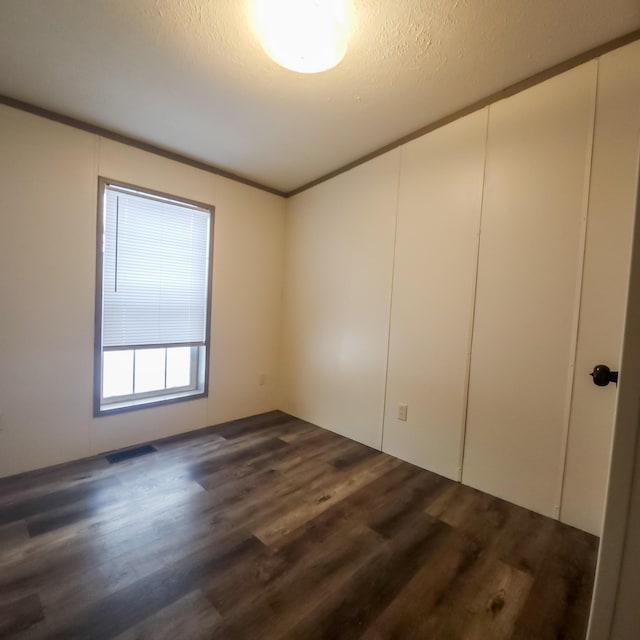 unfurnished room featuring crown molding, a textured ceiling, and dark wood finished floors