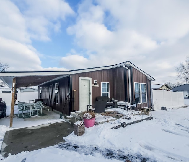 snow covered structure with an attached carport and fence