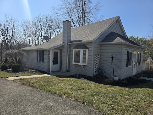 ranch-style home with a shingled roof, a front lawn, and a chimney