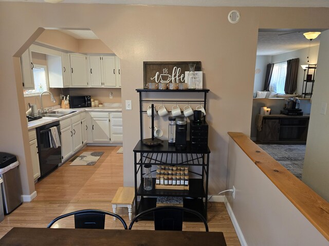 kitchen with black appliances, light wood-style flooring, a sink, white cabinets, and baseboards