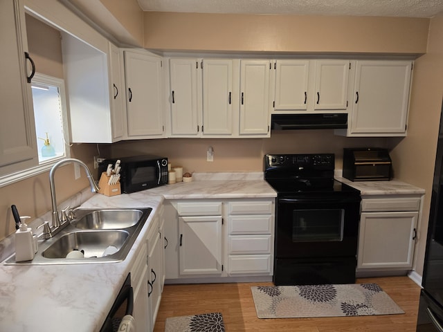 kitchen with light wood finished floors, a sink, black appliances, under cabinet range hood, and white cabinetry