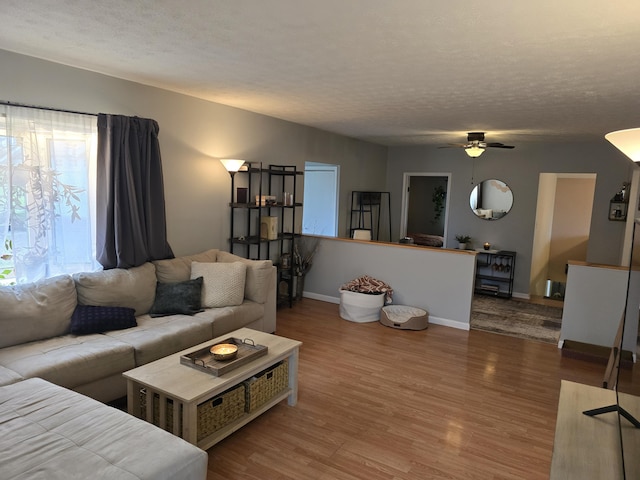 living room featuring a textured ceiling, wood finished floors, baseboards, and ceiling fan