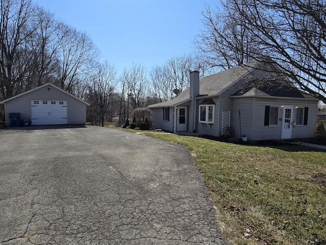 view of property exterior featuring a detached garage, aphalt driveway, a lawn, a chimney, and an outbuilding