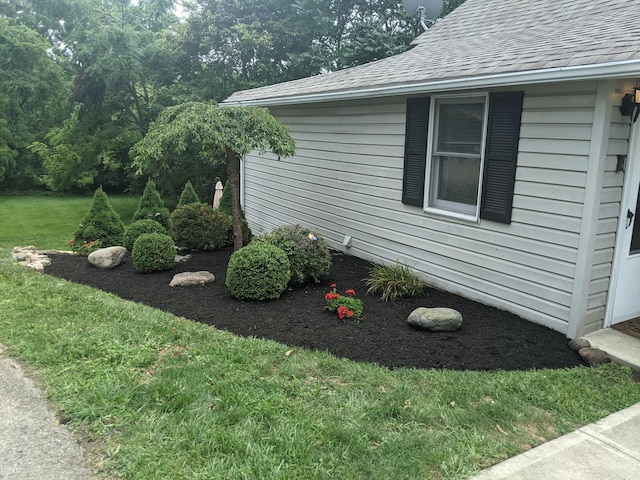 view of side of property with a lawn and roof with shingles