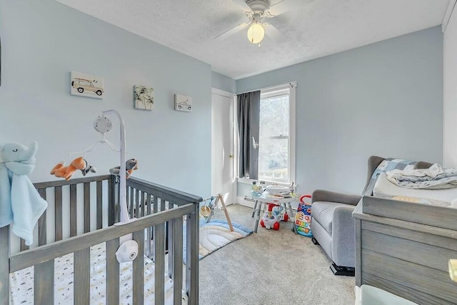 carpeted bedroom featuring a crib, a textured ceiling, and a ceiling fan