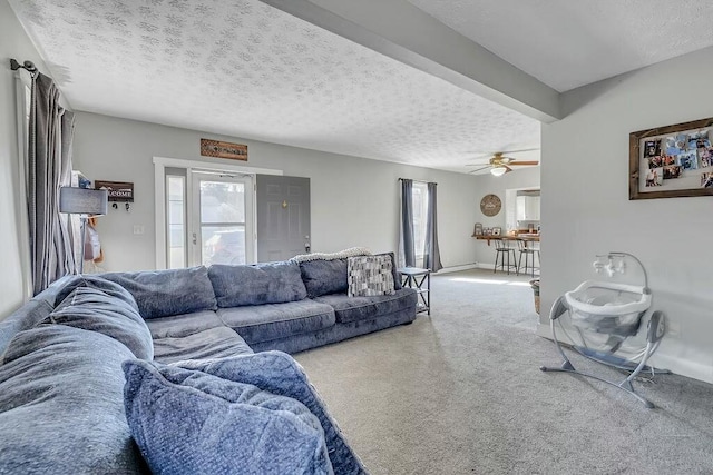 living area featuring baseboards, a textured ceiling, ceiling fan, and carpet flooring