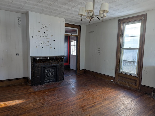 unfurnished living room with a fireplace, plenty of natural light, dark hardwood / wood-style flooring, and a chandelier