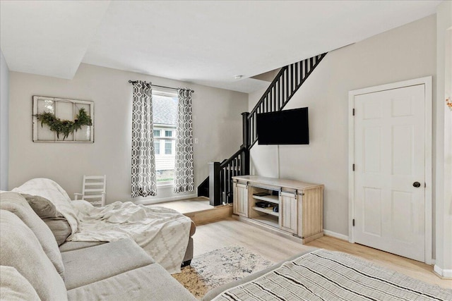 living area featuring baseboards, light wood-style flooring, and stairs