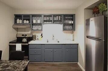 kitchen featuring under cabinet range hood, gray cabinetry, dark wood-type flooring, freestanding refrigerator, and electric range oven