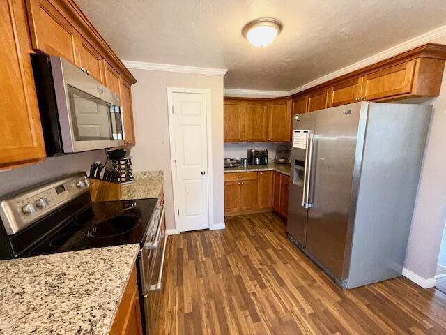 271 N Ludlow St, Covington, OH 45318 - kitchen with stainless steel appliances, brown cabinetry, crown molding, dark wood finished floors, and light stone counters
