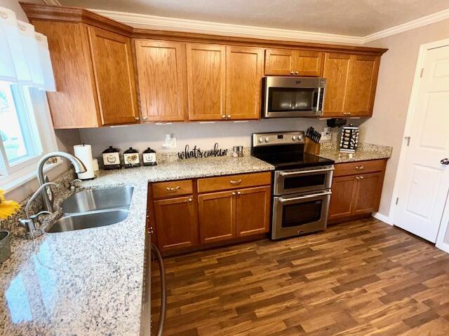 271 N Ludlow St, Covington, OH 45318 - kitchen featuring appliances with stainless steel finishes, crown molding, brown cabinets, dark wood-type flooring, and light stone countertops