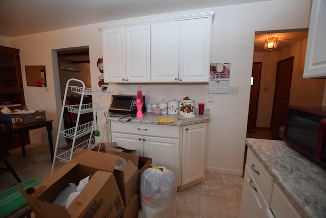 kitchen featuring white cabinets, a wall mounted air conditioner, and light stone counters