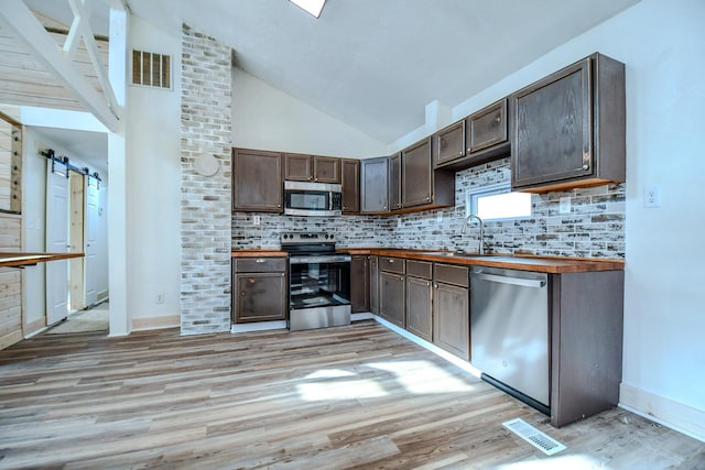 kitchen featuring butcher block countertops, sink, stainless steel appliances, a barn door, and dark brown cabinets