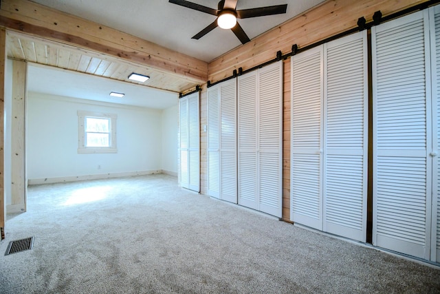 unfurnished bedroom featuring a closet, beamed ceiling, ceiling fan, a barn door, and carpet