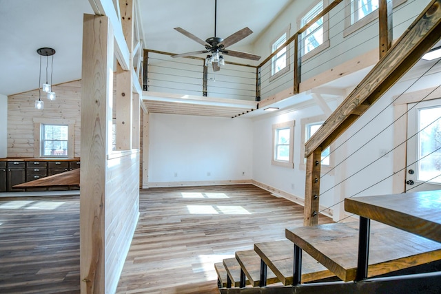 unfurnished living room with a high ceiling, ceiling fan, hardwood / wood-style floors, and wooden walls