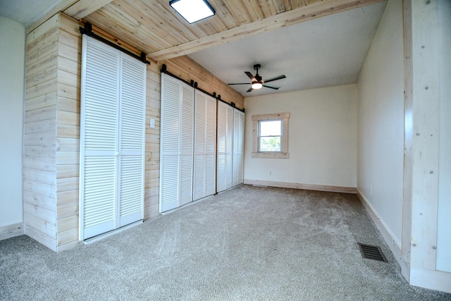 unfurnished bedroom with beamed ceiling, light colored carpet, a barn door, and multiple closets