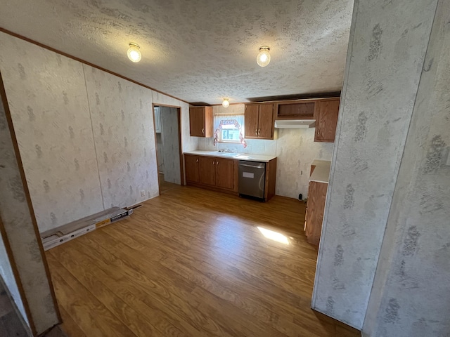 kitchen with brown cabinetry, wood finished floors, light countertops, a textured ceiling, and dishwasher