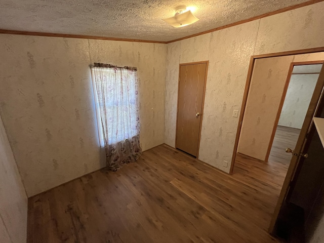 unfurnished bedroom featuring wood finished floors, a textured ceiling, ornamental molding, and a textured wall