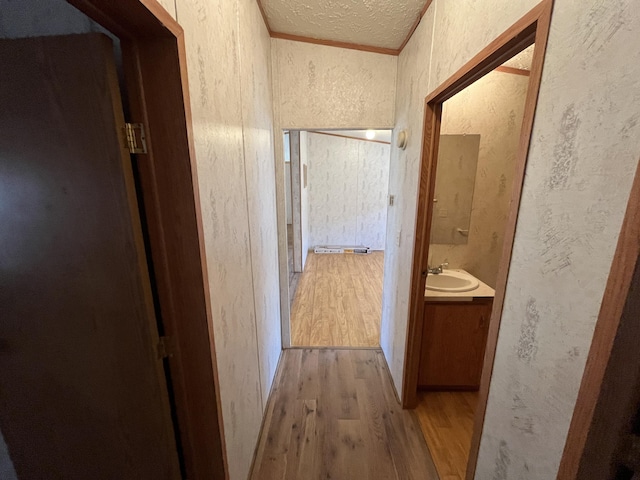 hall with a sink, a textured ceiling, a textured wall, and wood finished floors