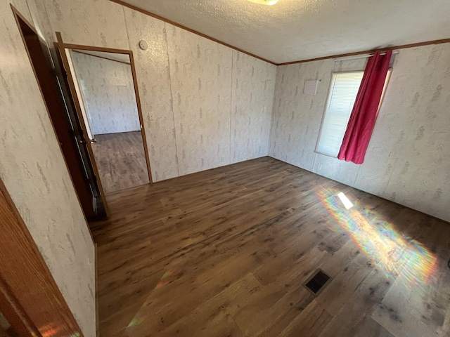 empty room featuring dark wood finished floors, visible vents, a textured ceiling, and crown molding