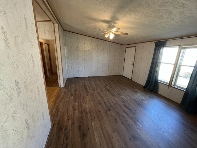 empty room featuring a textured ceiling, ornamental molding, dark wood-style flooring, and a textured wall