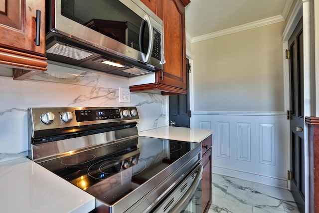 kitchen featuring a wainscoted wall, marble finish floor, appliances with stainless steel finishes, crown molding, and light countertops