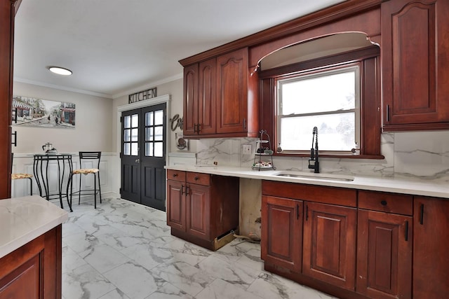 kitchen featuring a wainscoted wall, marble finish floor, a sink, crown molding, and light countertops