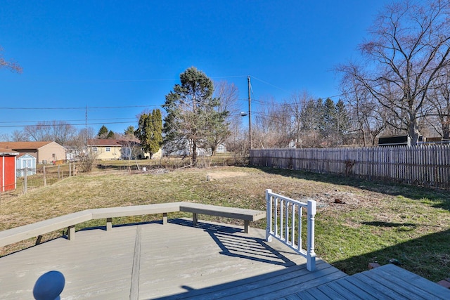 wooden deck featuring a yard, an outdoor structure, a fenced backyard, and a shed