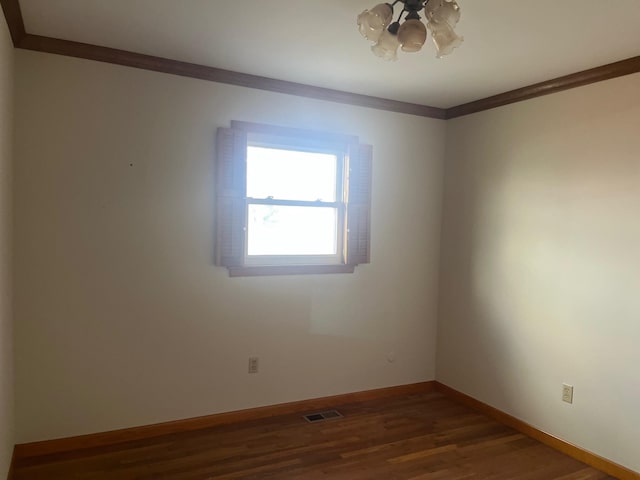 empty room with crown molding, wood finished floors, visible vents, and baseboards