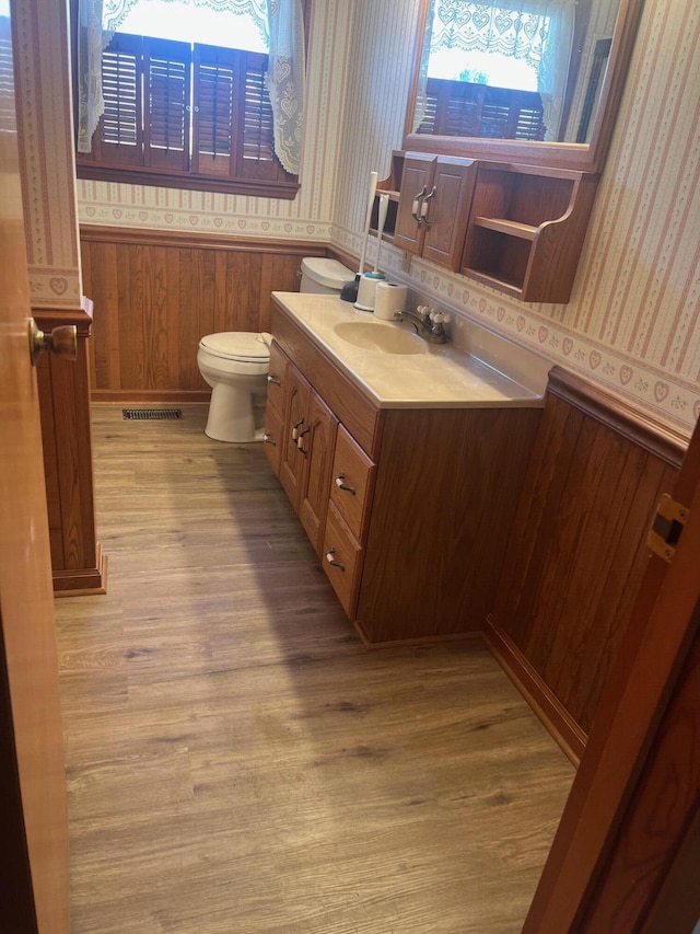 half bath with a wainscoted wall, visible vents, toilet, and wallpapered walls