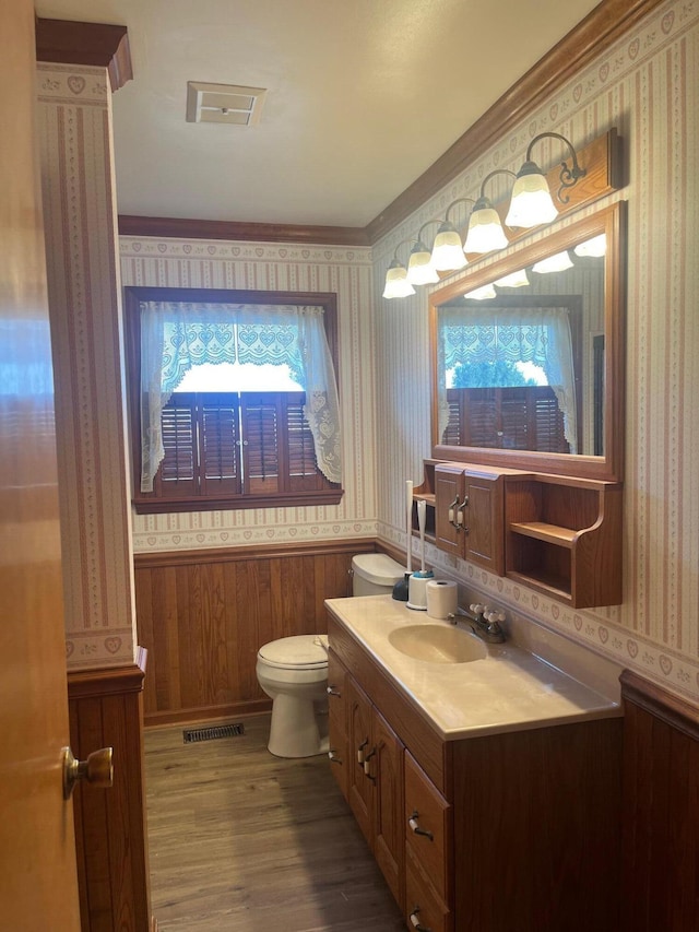 half bathroom with visible vents, toilet, vanity, wood finished floors, and wallpapered walls