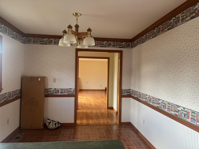 hall featuring a notable chandelier, brick patterned floor, wainscoting, and wallpapered walls