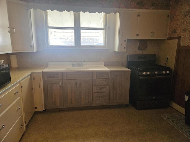 kitchen with a sink, wallpapered walls, light countertops, and black gas stove