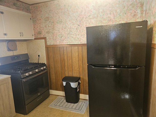 kitchen with wallpapered walls, black appliances, light countertops, wainscoting, and white cabinetry