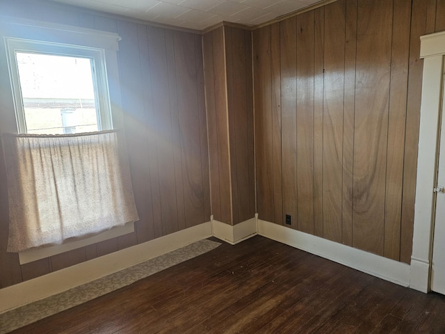 unfurnished room with baseboards, dark wood finished floors, and wood walls