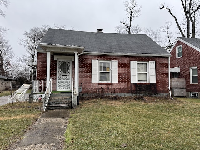 view of front of property with roof with shingles, brick siding, a front lawn, and a chimney