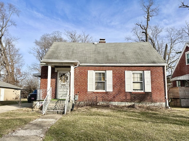 view of front facade with roof with shingles, brick siding, a front lawn, and a chimney