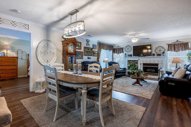 dining area with a tile fireplace, a textured ceiling, dark wood-type flooring, and ornamental molding