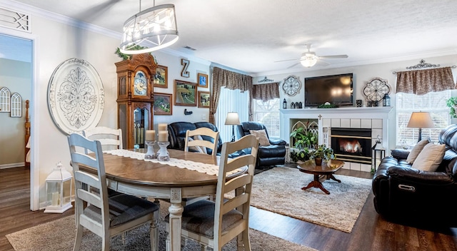 dining room featuring baseboards, a tiled fireplace, ornamental molding, ceiling fan with notable chandelier, and wood finished floors