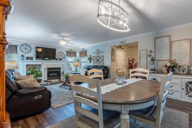 dining space featuring dark wood finished floors, ornamental molding, ceiling fan with notable chandelier, and a tile fireplace