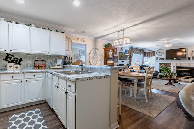 kitchen with a peninsula, white dishwasher, a sink, ornamental molding, and open floor plan