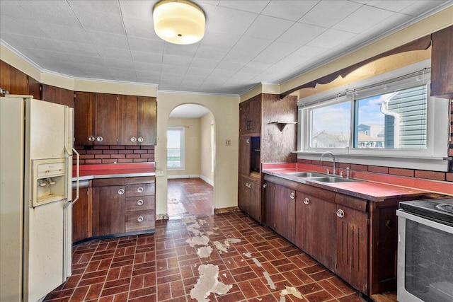 kitchen with crown molding, range, sink, and white fridge with ice dispenser