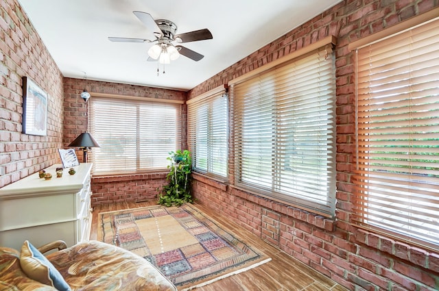 sitting room with ceiling fan, brick wall, wood-type flooring, and a wealth of natural light