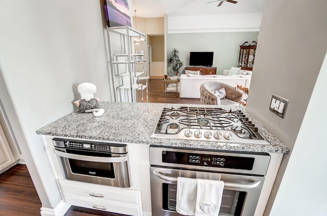 kitchen with white cabinets, dark hardwood / wood-style flooring, ceiling fan, stainless steel appliances, and light stone countertops