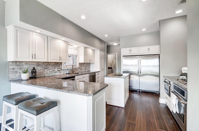 kitchen featuring appliances with stainless steel finishes, sink, white cabinets, a center island, and kitchen peninsula